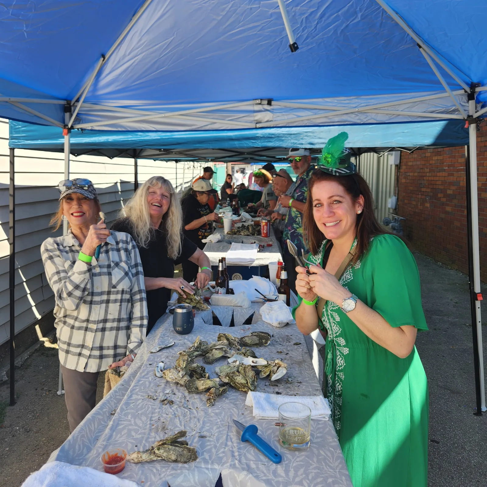 People smiling around an outdoor table of oysters under blue canopies